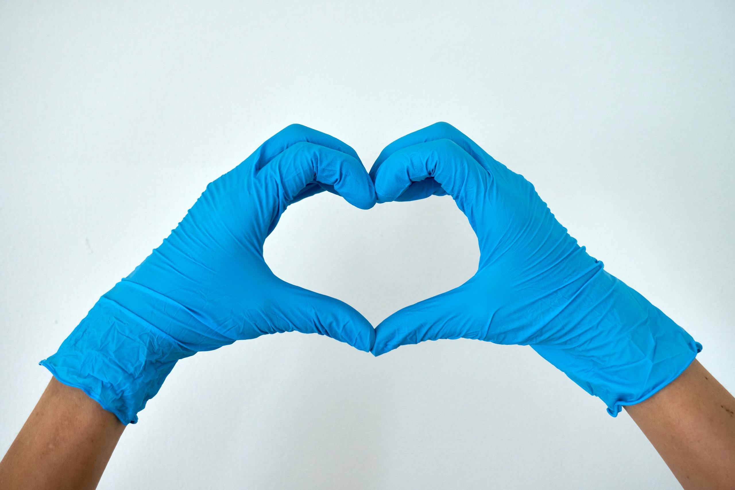 Hands wearing blue gloves forming a heart shape, symbolizing healthcare support and love.